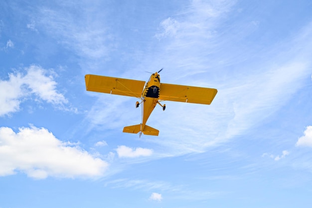 Avião amarelo monomotor ultraleve voando no céu azul com nuvens brancas