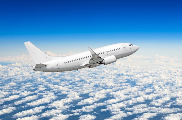 Avião branco voa alto no céu acima do céu azul de nuvens.