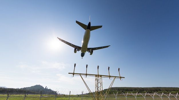 Avião com chassi voando sobre um céu azul, luz de navegação ou aterrissagem que conduz à pista no fundo, grande angular