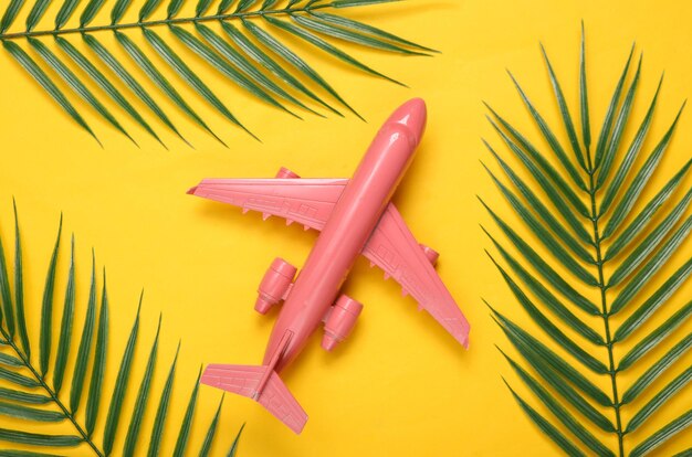 Avião de ar e folhas verdes de palma em fundo amarelo Conceito de viagem Composição tropical Vista superior Configuração plana