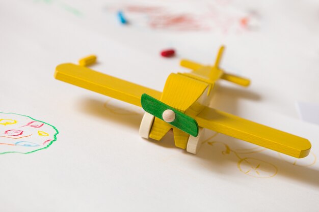 Foto avião de brinquedo de madeira amarelo sobre fundo branco com desenhos de crianças