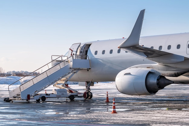 Avião de passageiros branco com escada de embarque de passageiros no avental de inverno frio do aeroporto