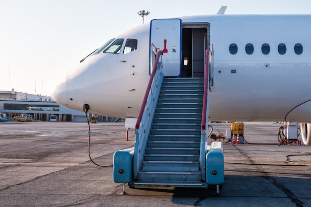 Avião de passageiros com escada de embarque no pátio do aeroporto e conectado a uma fonte de alimentação externa