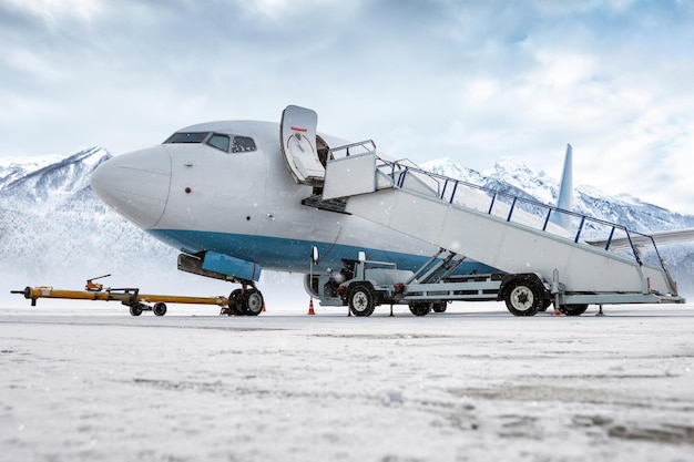 Avião de passageiros com escadas aéreas em uma nevasca no fundo de altas montanhas cobertas de neve