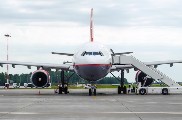 Avião de passageiros no estacionamento no aeroporto com um nariz para a frente e um corredor.