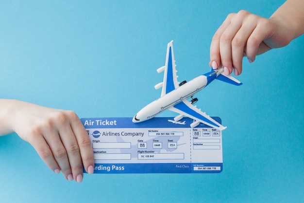 Avião e passagem aérea na mão da mulher sobre um fundo azul. Conceito de viagens, copie o espaço.