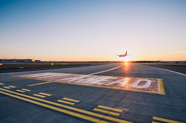 Foto avião em frente à pista de pouso a aterrar no aeroporto durante o pôr do sol