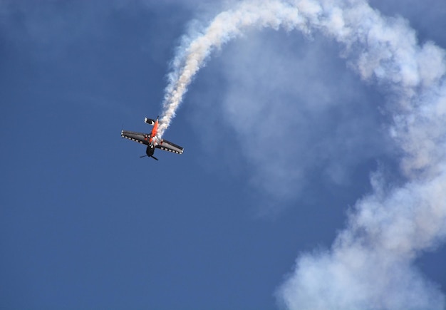 Avião militar voa com fumaça no céu azul