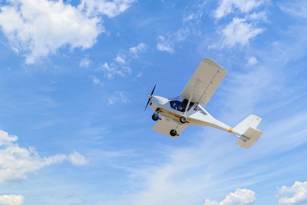 Avião ultraleve monomotor voando no céu azul com nuvens brancas