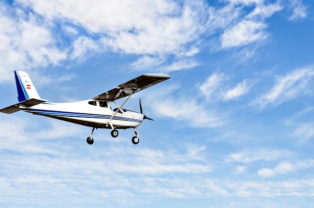 Avião ultraleve monomotor voando no céu azul com nuvens brancas.