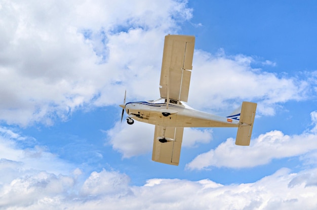 Avião ultraleve monomotor voando no céu azul com nuvens brancas.