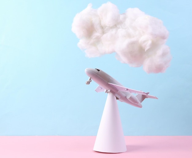 Avión de aire de juguete con una nube esponjosa flotante sobre un fondo azul pastel rosa Arte conceptual Idea de viaje minimalista