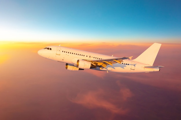 Avión alto en el cielo vuela sobre las nubes durante la luz del atardecer y el atardecer.