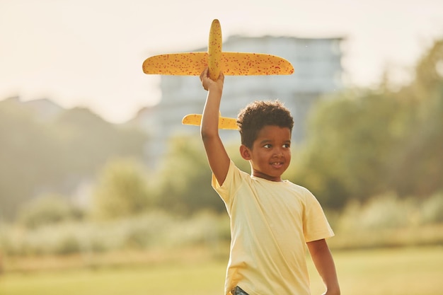 Avión amarillo en las manos Un niño afroamericano se divierte en el campo durante el día de verano