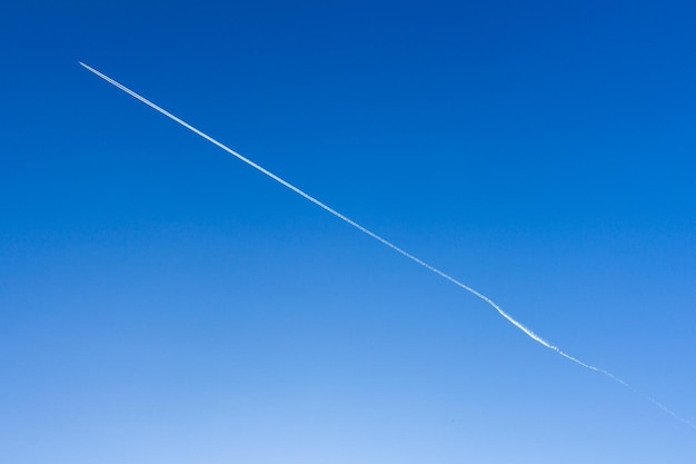 El avión en el cielo azul deja rayas blancas detrás de él.