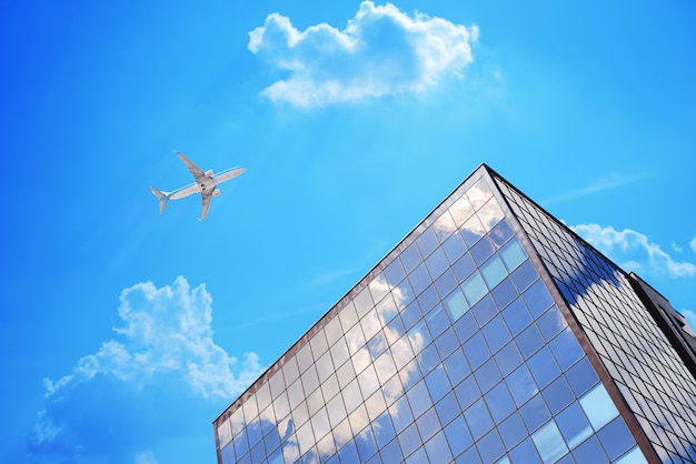 Avión en el cielo azul con nubes cerca del moderno edificio de oficinas o aeropuerto