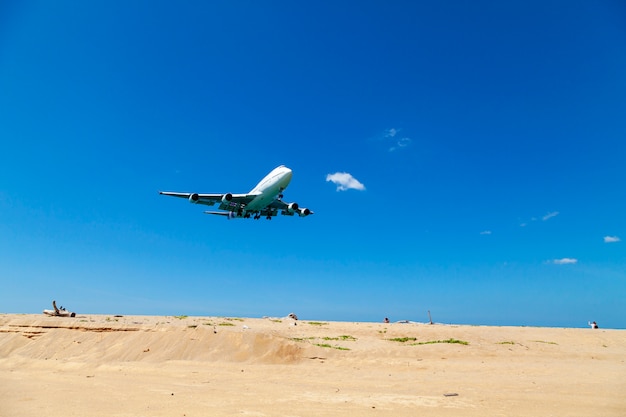 Avión comercial aterrizando sobre mar y cielo azul claro.