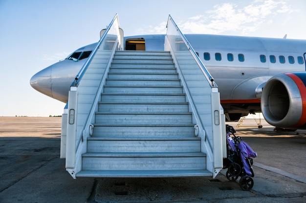 Avión con escalones de embarque de pasajeros en la plataforma del aeropuerto con un cochecito preparado para el transporte de niños
