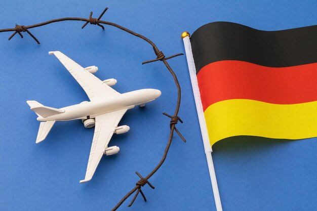 Avión de juguete, bandera de Alemania y alambre de púas sobre fondo azul, concepto de seguridad fronteriza aérea del país