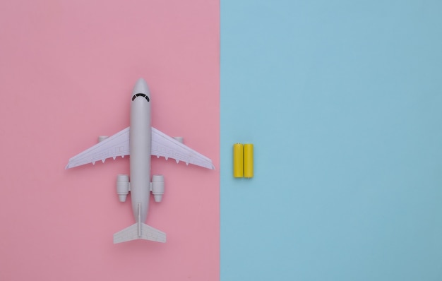 Avión de juguete y baterías sobre un fondo pastel azul-rosa. Vista superior