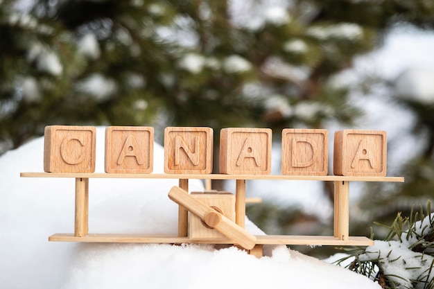 Avión de juguete de madera y la inscripción Canadá hecha de cubos de madera en el fondo de un bosque nevado. El concepto de viajar a países de invierno, a Canadá. estilo retro, vendimia