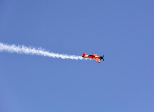 Avión militar vuela con humo en el cielo azul