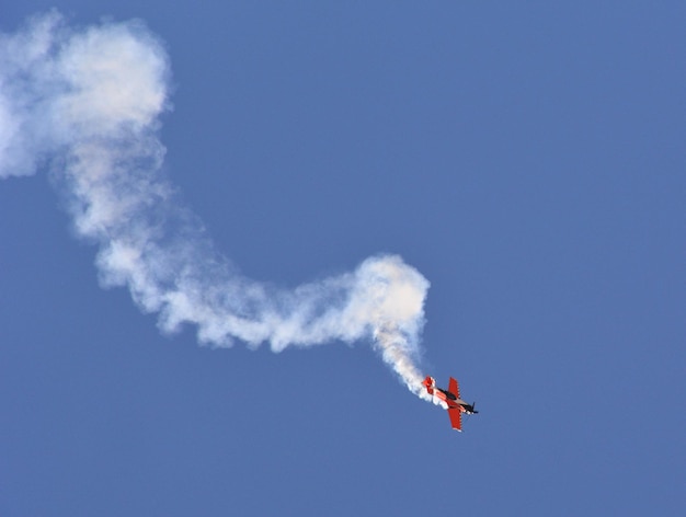 Avión militar vuela con humo en el cielo azul