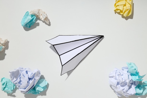 Avión de papel y bolas de papel sobre fondo blanco.