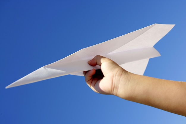 Avión de papel en mano de niños sobre cielo azul