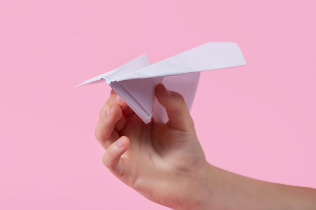 Avión de papel en la mano de los niños sobre un fondo rosa juegos de viaje con bebé