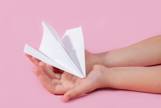 Avión de papel en la mano de los niños sobre un fondo rosa juegos de viaje con bebé