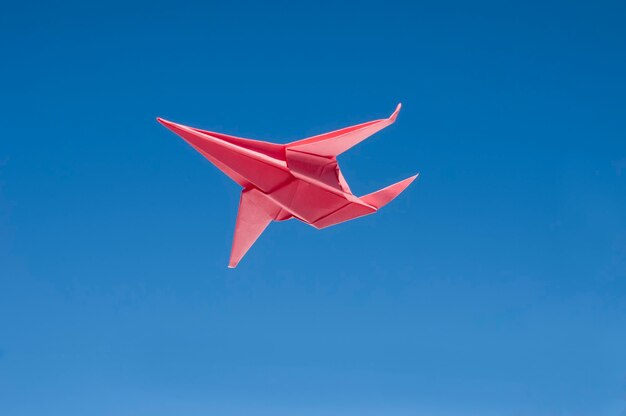 Avión de papel rojo volando aislado en azul