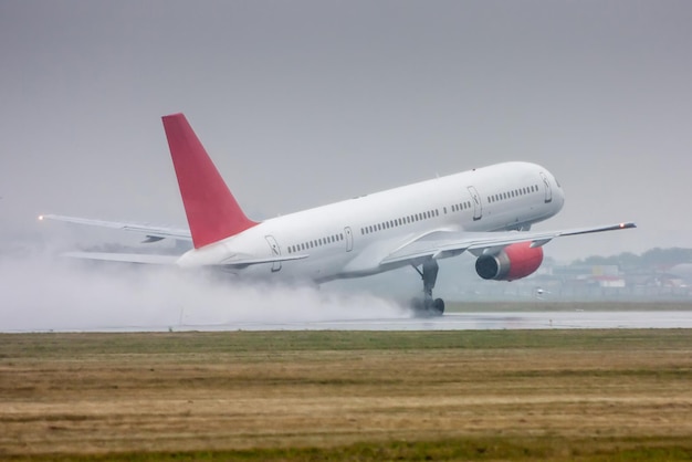 Un avión de pasajeros blanco se mueve en la pista bajo una lluvia intensa. Despegue con spray fuerte