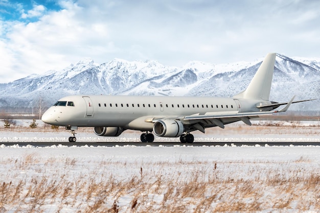 Avión de pasajeros blanco en la pista del aeropuerto de invierno en el fondo de altas montañas escénicas