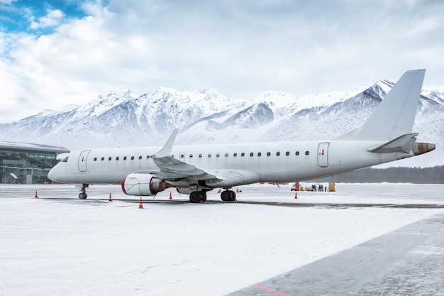 Avión de pasajeros blanco en la plataforma del aeropuerto con el telón de fondo de montañas nevadas