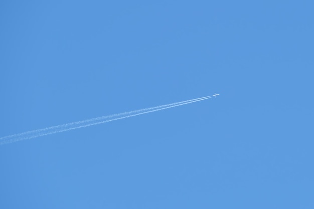 Avión de pasajeros distante que volaba a gran altura en un cielo azul claro dejando un rastro de humo blanco detrás del concepto de transporte aéreo