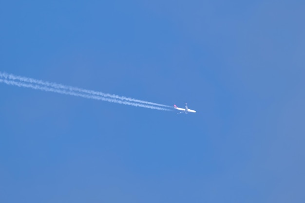 Avión de pasajeros distante que volaba a gran altura en un cielo azul claro dejando un rastro de humo blanco detrás de la estela. concepto de transporte aéreo