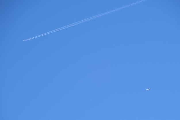 Foto avión de pasajeros distante volando a gran altitud en el cielo azul claro dejando rastro de humo blanco de estela detrás. concepto de transporte aéreo.