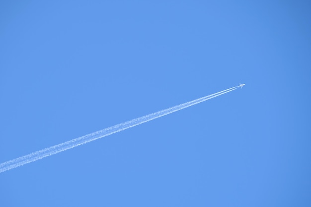 Avión de pasajeros distante volando a gran altura en el cielo azul claro dejando rastro de humo blanco de estela detrás. Concepto de transporte aéreo.