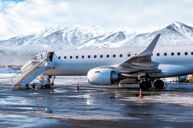 Avión de pasajeros con escaleras de embarque en invierno en el fondo de altas montañas pintorescas