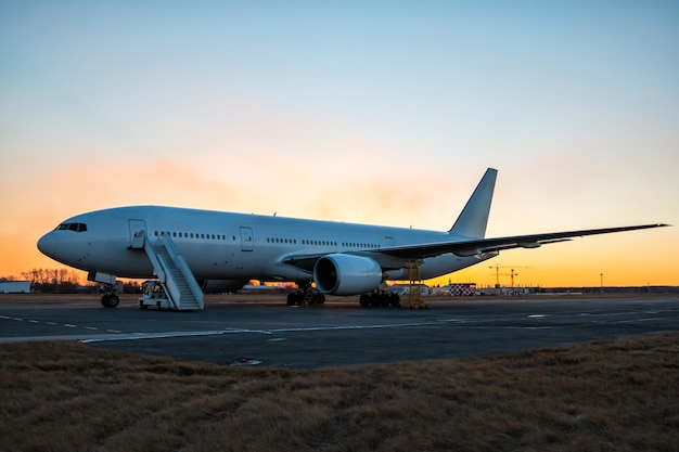 Avión de pasajeros de fuselaje ancho blanco con escalones de embarque en la plataforma del aeropuerto en el crepúsculo vespertino