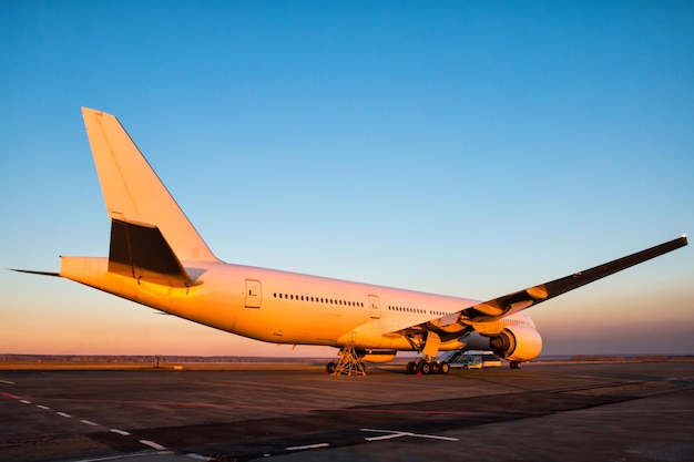 Avión de pasajeros de fuselaje ancho blanco en la plataforma del aeropuerto en la luz del atardecer