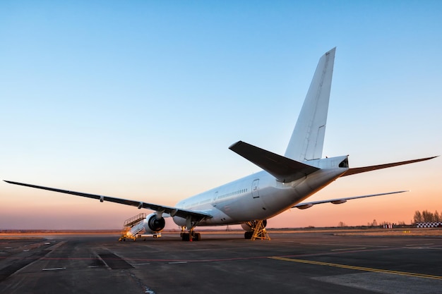 Avión de pasajeros de fuselaje ancho blanco en la plataforma del aeropuerto en la luz del atardecer