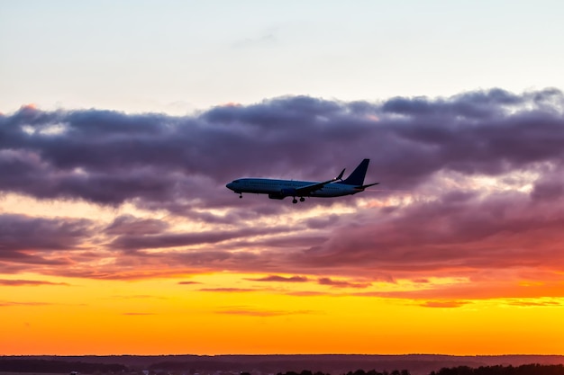 Avión de pasajeros temprano en la mañana aterrizando con el telón de fondo de un colorido cielo del amanecer