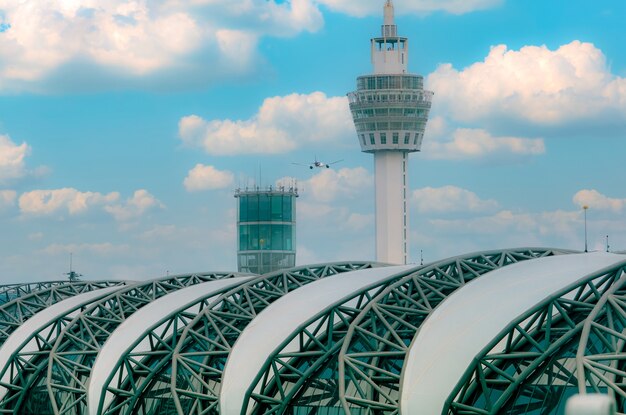 Avión de pasajeros volando por encima del edificio del aeropuerto Edificio del aeropuerto y torre de control del tráfico aéreo