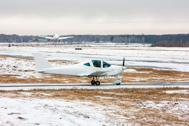 Avión pequeño se mueve en la calle de rodaje y detrás del avión despega en un aeródromo de invierno frío