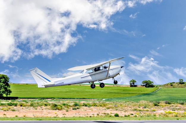 Avión ultraligero de un solo motor despegando del aeródromo bajo un cielo azul con nubes blancas.