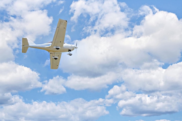 Avión ultraligero de un solo motor volando en el cielo azul con nubes blancas.