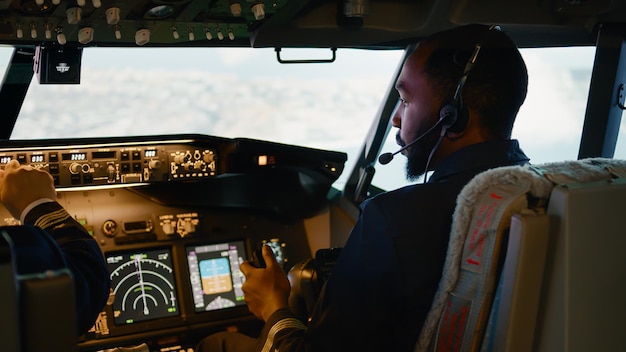 Foto avión volador copiloto afroamericano con capitán en cabina, mango de motor estrangulador y fijación de altitud y longitud. mando de navegación en salpicadero y panel de control.