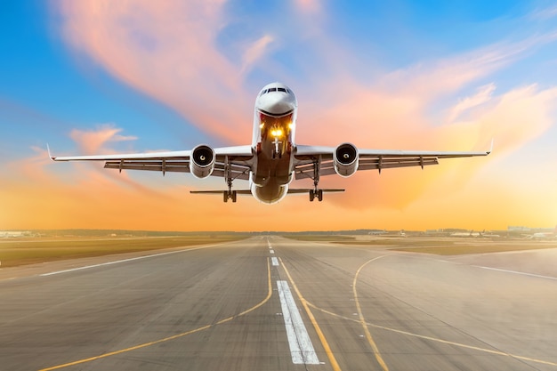 Avión volando llegada aterrizando en una pista por la noche durante una puesta de sol de color rojo brillante.